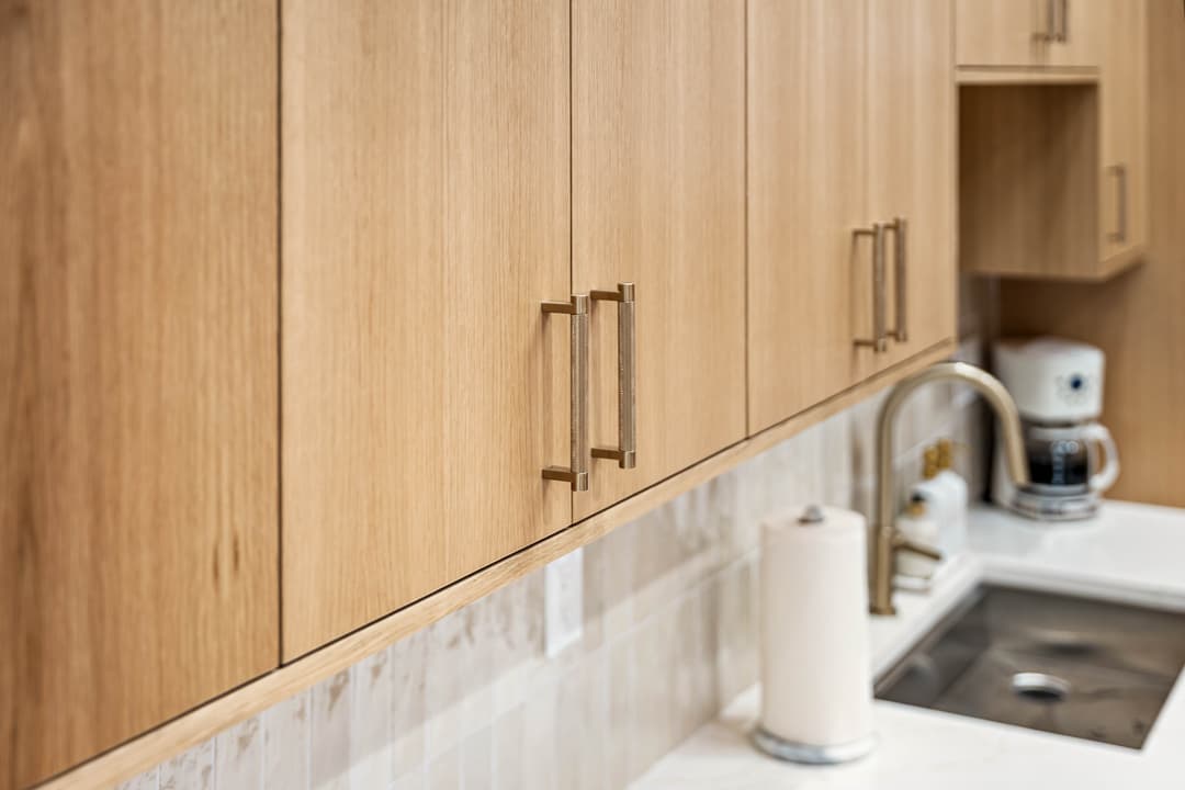 Modern kitchen with oak cabinets, gold handles, and sleek sink with white marble countertop.