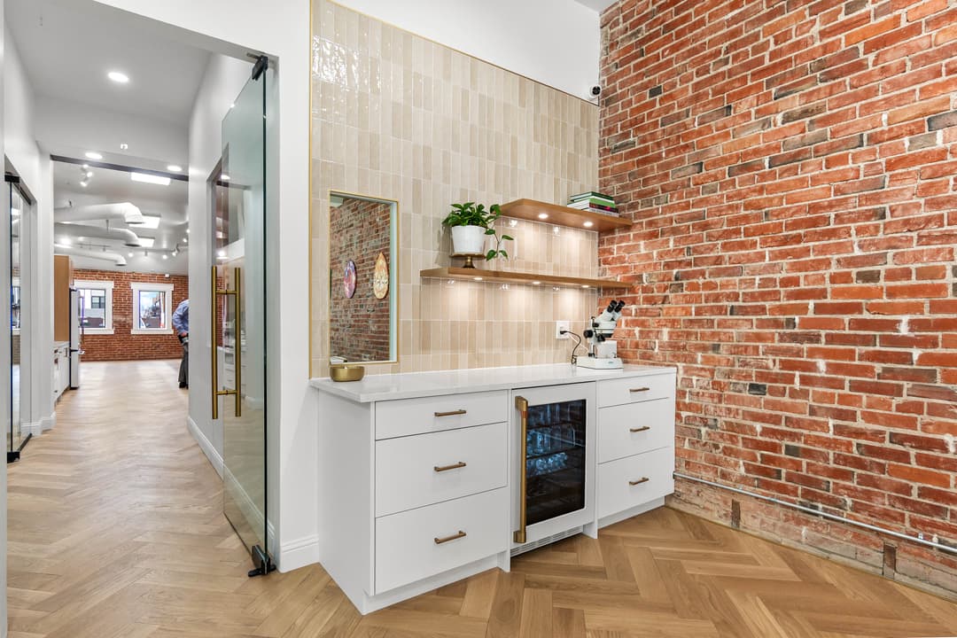 Modern kitchen corner with white cabinets, brick wall, shelving, and a wine cooler.