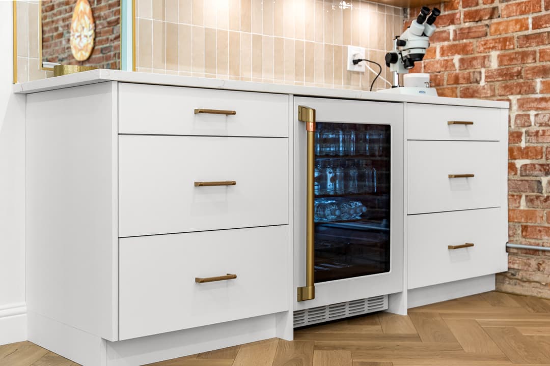 Modern white kitchen cabinetry with a glass-front beverage fridge and brick accent wall.