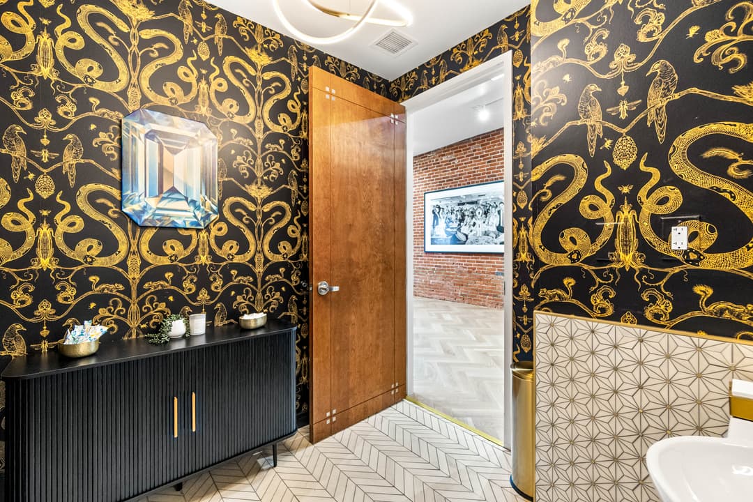 Stylish bathroom with gold patterned wallpaper, a dark cabinet, and modern decor elements.