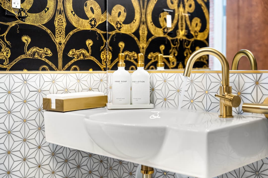 Stylish bathroom sink with gold accents, soap and lotion bottles, and decorative wall design.