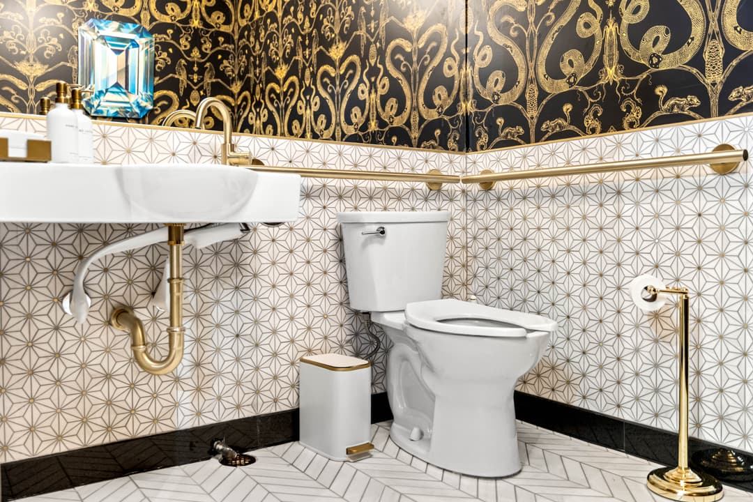 Luxurious bathroom featuring gold accents, elegant wallpaper, and modern fixtures.