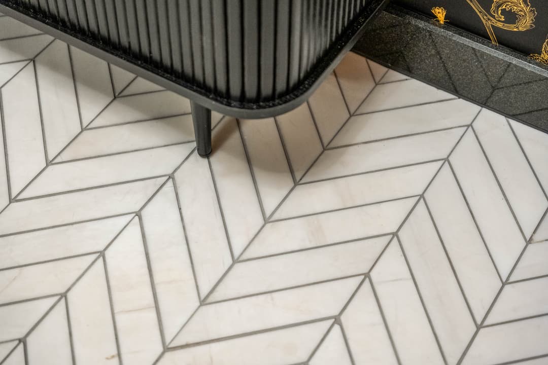 Stylish black cabinet on herringbone patterned marble floor in modern interior design.