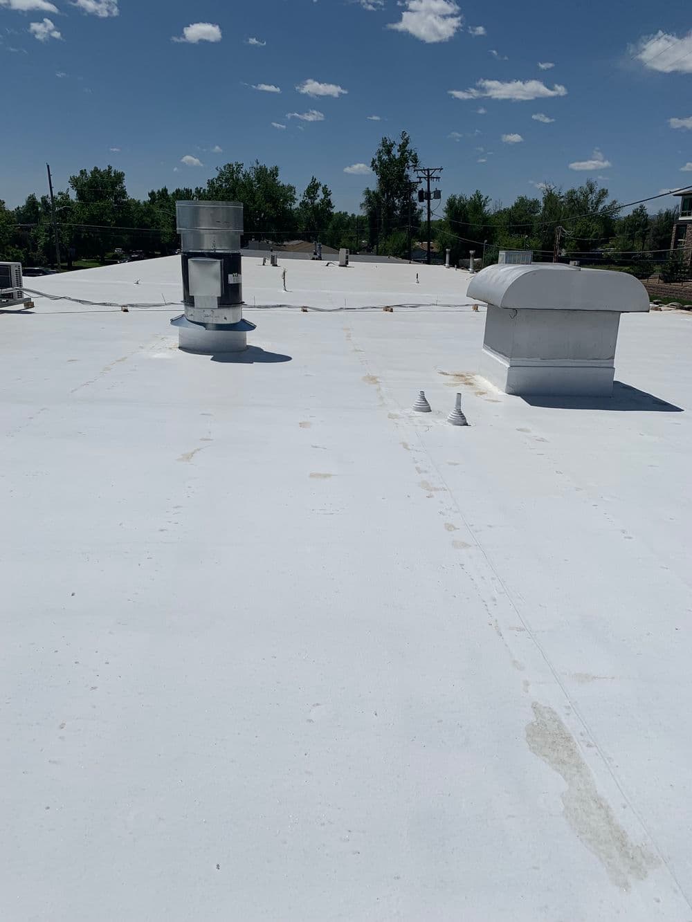 Flat white commercial roof with vents and clear blue sky, showcasing maintenance potential.