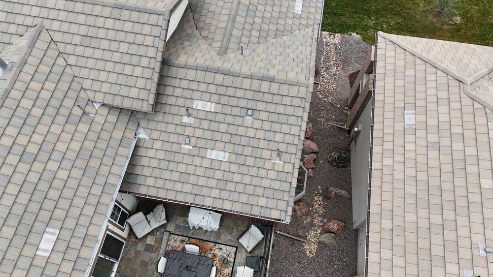 Aerial view of residential rooftops with gray shingles and outdoor seating area visible.