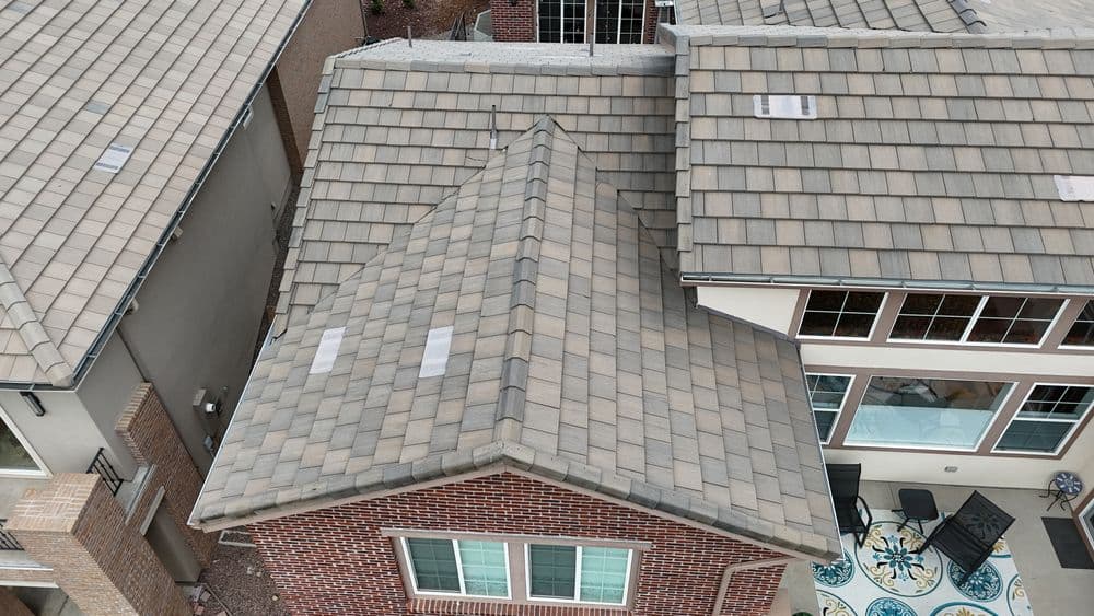 Aerial view of residential roofing with shingles on a modern home and patio area.