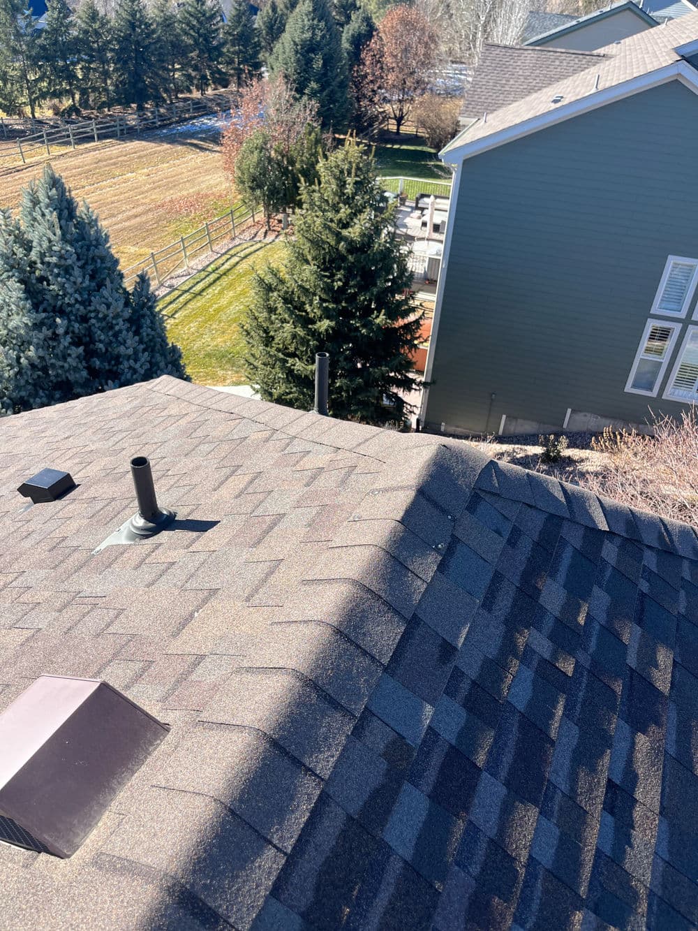 Aerial view of a rooftop with shingles, chimney, and surrounding trees and houses.