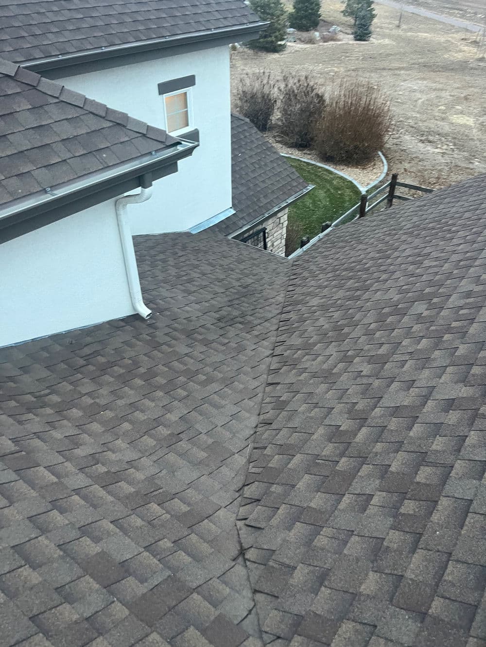 Bird's-eye view of a brown shingle roof with a sloped design and nearby landscaping.