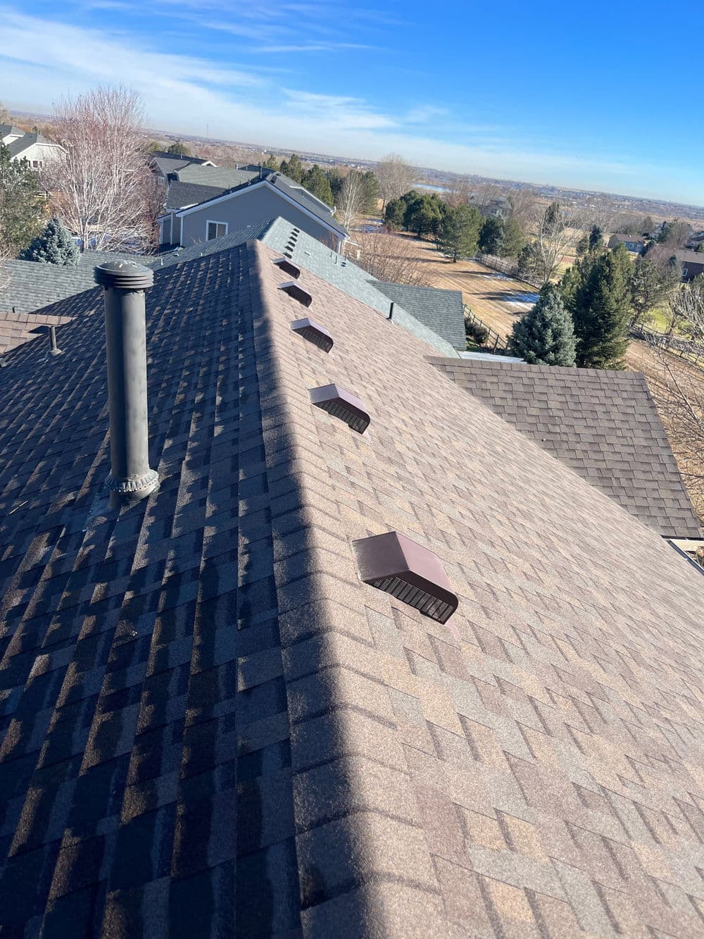 Roof view with vents on a residential neighborhood under a clear blue sky.
