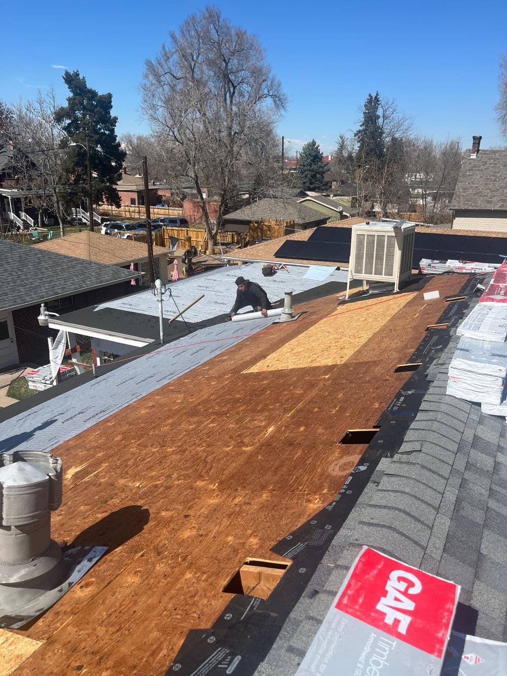 Roofing installation with workers, showing new shingles and underlayment on residential homes.