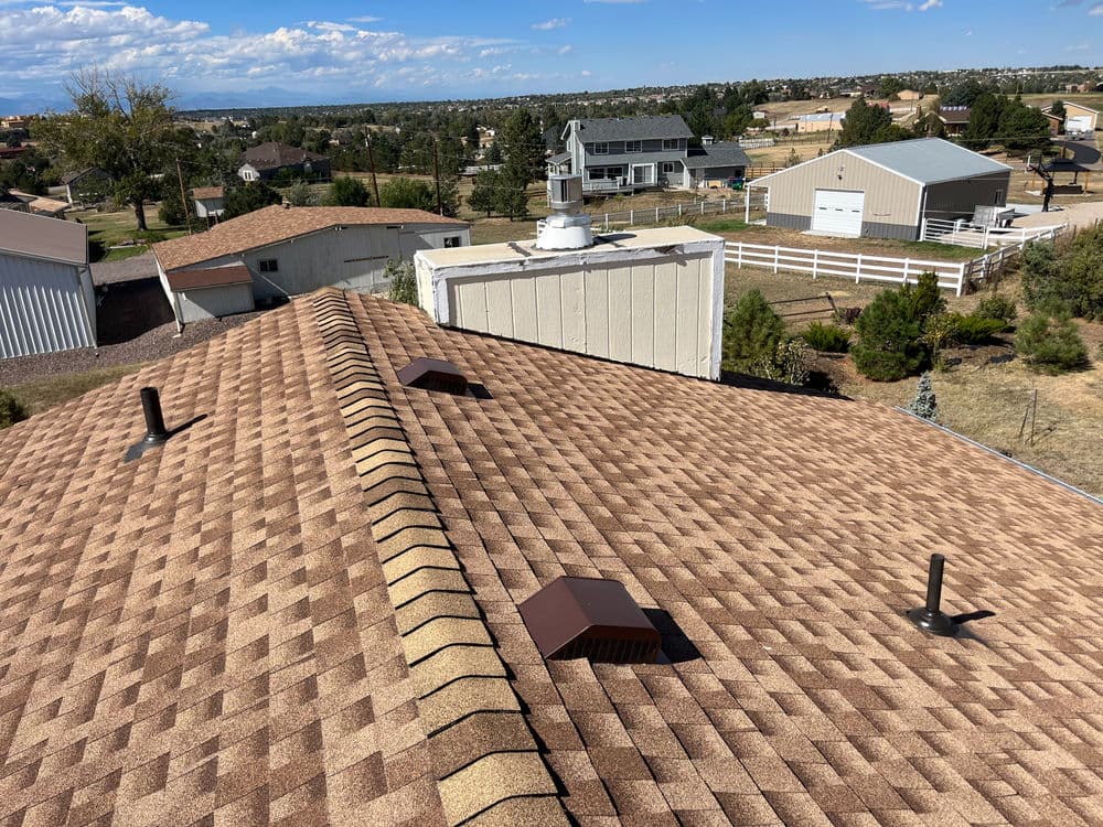 Overview of a residential roof with asphalt shingles and ventilation features in a scenic landscape.