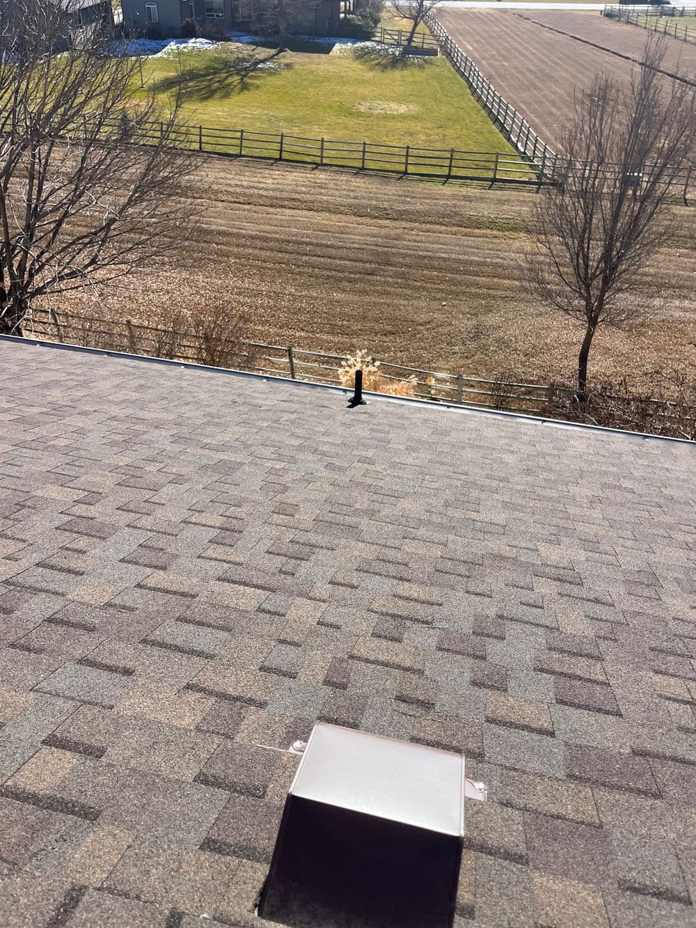 View from a rooftop showing a vent and fields with a fence in the background.