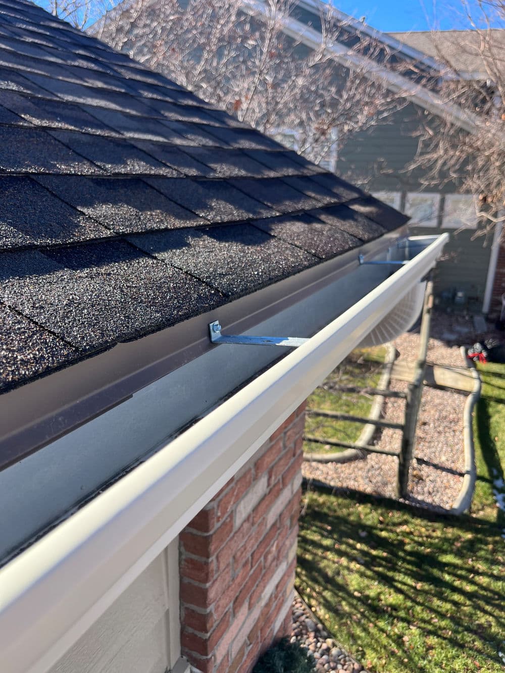 Close-up of a gray gutter on a house with a shingled roof and green grass below.