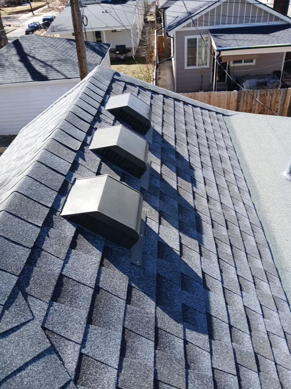 Three roof vents on a sloped shingles roof, with shadows creating visual contrast.