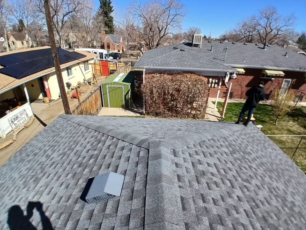 Aerial view of residential rooftops with solar panels and a person inspecting a roof.