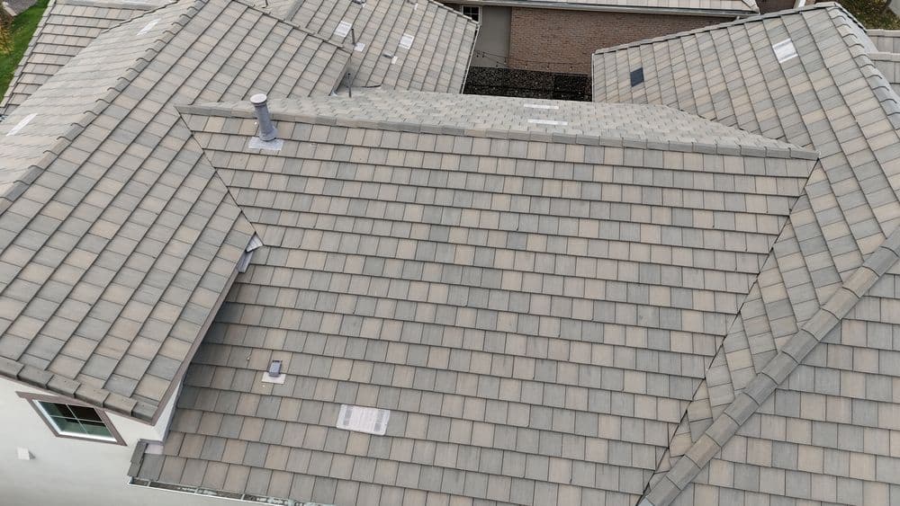 Aerial view of a modern home roof with gray tiles and chimney, showcasing roofing texture.